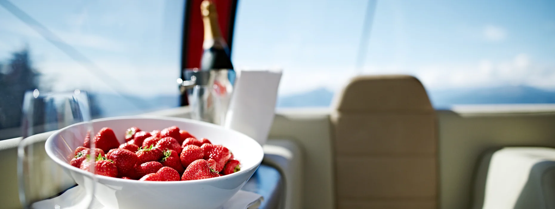 Primo piano: ciotola di fragole fresche, bottiglia di champagne e calici nella cabinovia VIP