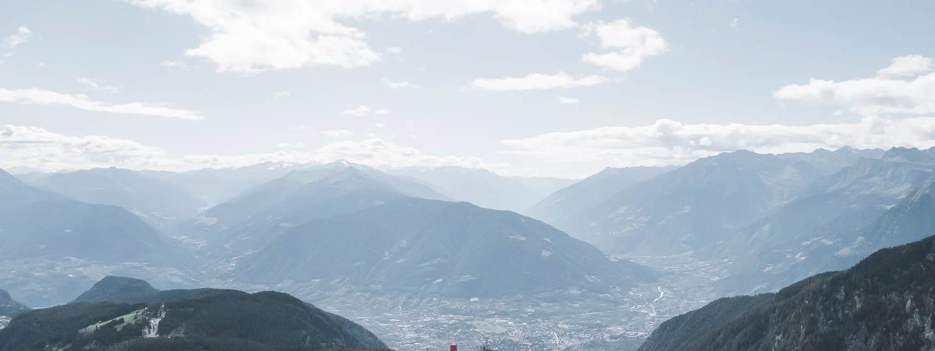 Vista panoramica su prati alpini verdi e la Val d'Adige dell'Alto Adige con catene montuose sullo sfondo