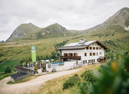 Rifugio Merano in estate con terrazza soleggiata, ombrelloni e paesaggio montano verde