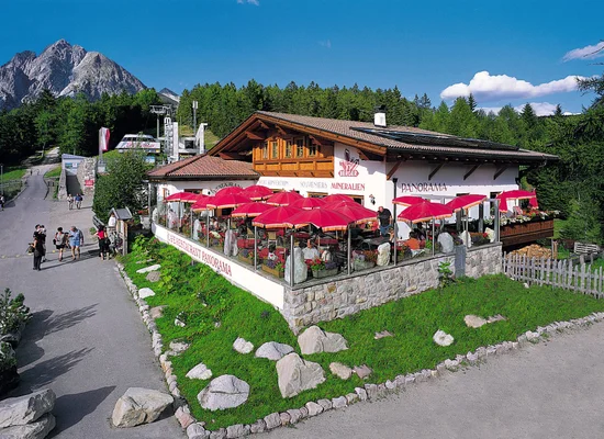 Café Restaurant Panorama con ombrelloni rossi sulla terrazza, paesaggio montano e stazione funiviaria in estate