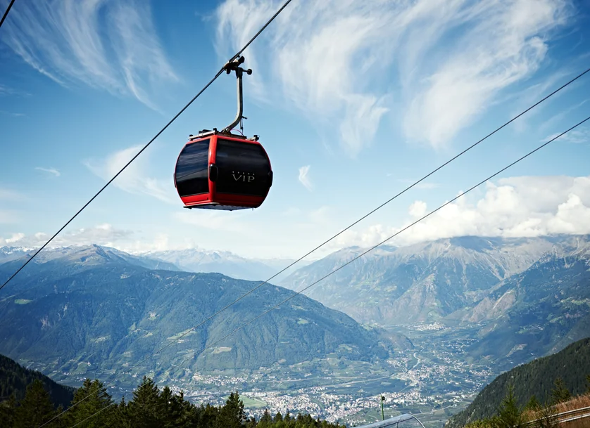 Cabinovia VIP rosso-nera sospesa sopra la Valle di Merano con panorama montano in estate